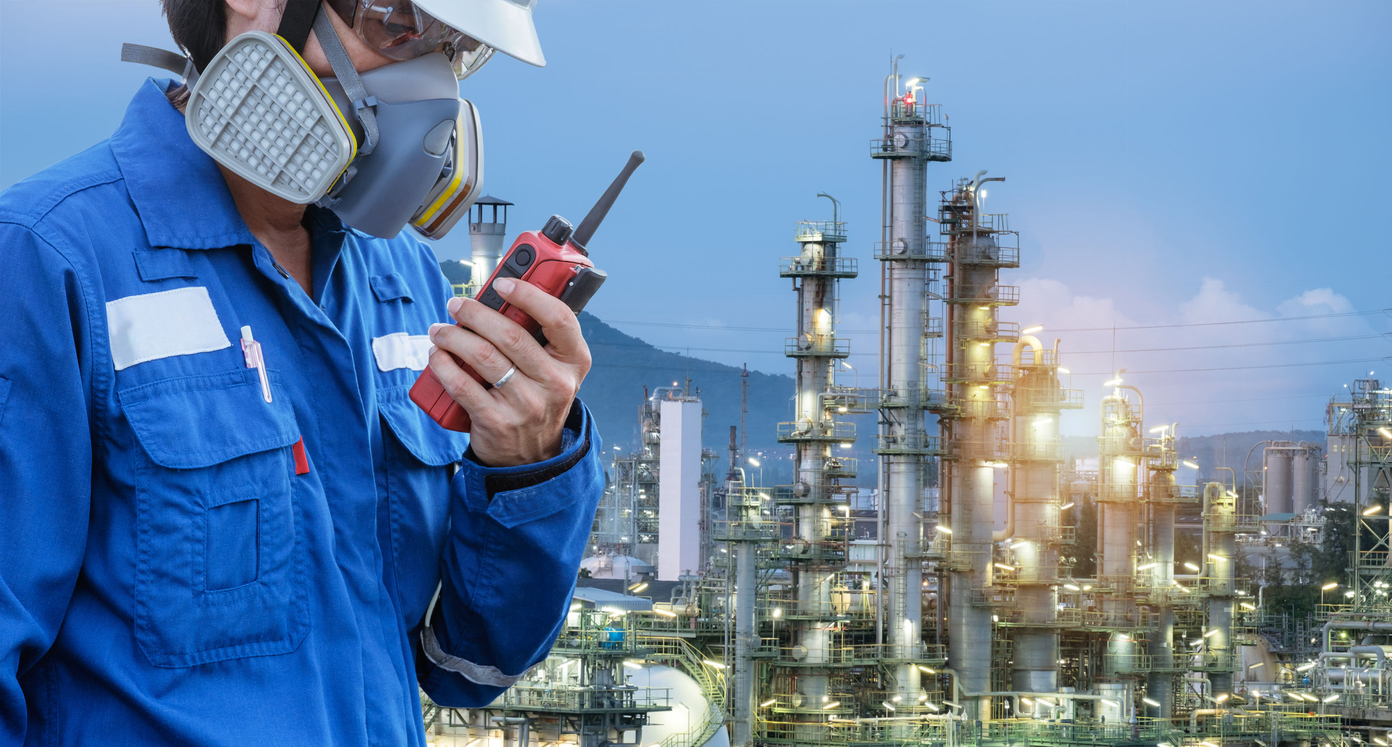 Un homme portant un masque respiratoire et une combinaison bleue parle dans un walky-talky dans un environnement industriel